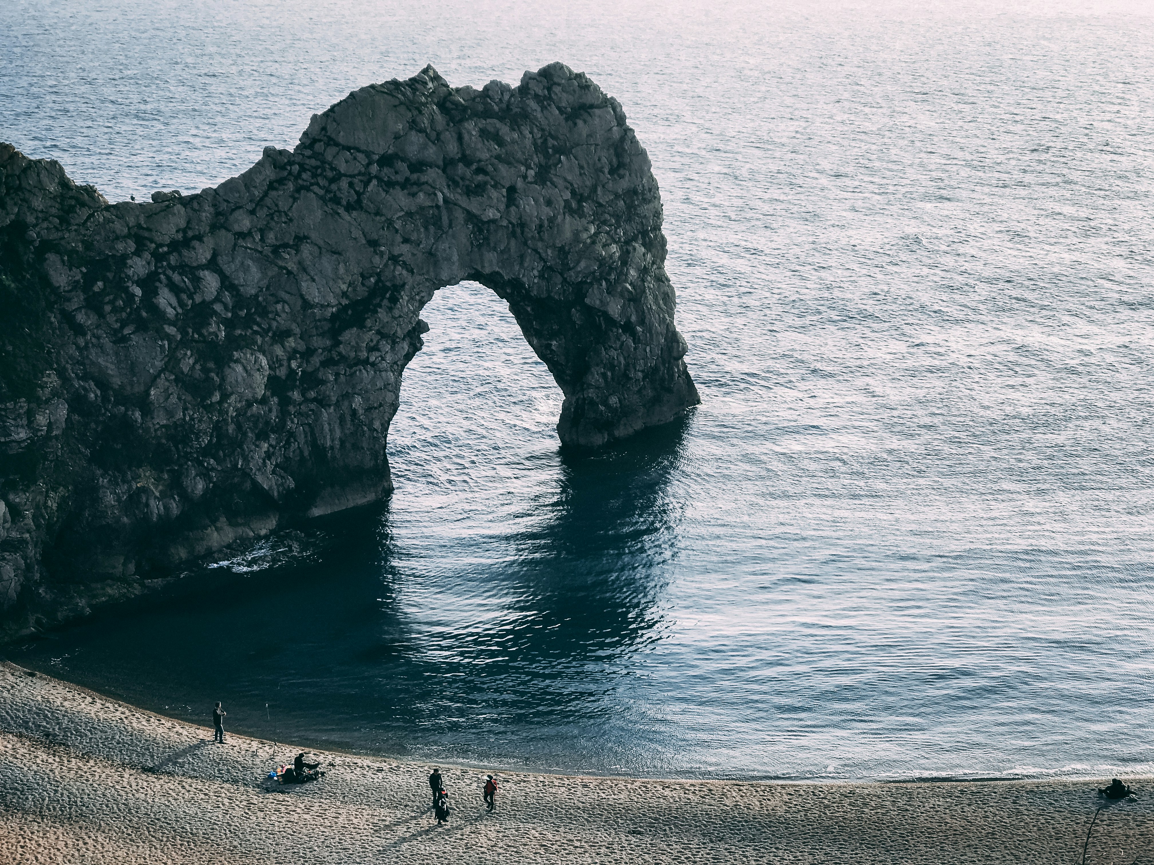 four persons standing on seashore near rock form of arch